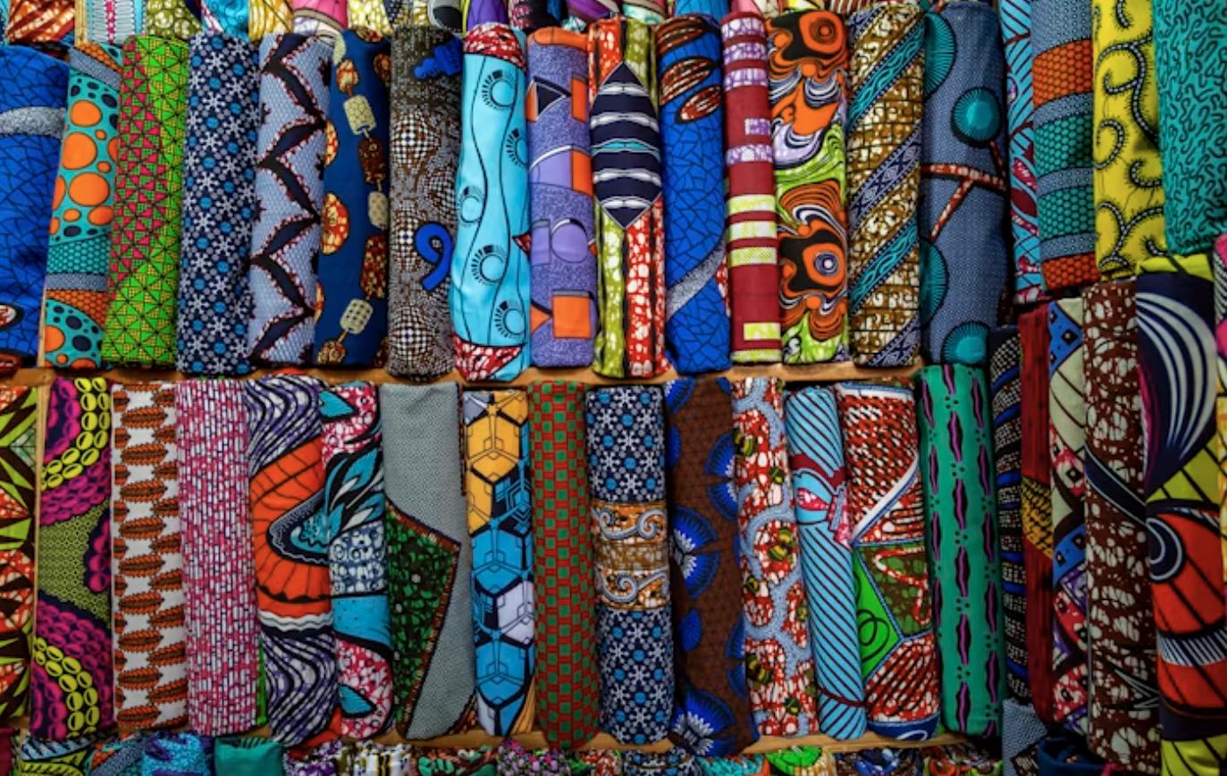 Rows of colorful African wax print fabrics rolled and stacked at a textile market